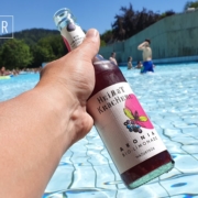 Heimat-Kracherl-Bio-Limonade-01 Eine Flasche Heimat Kracherl in der Hand vor einem Freibad